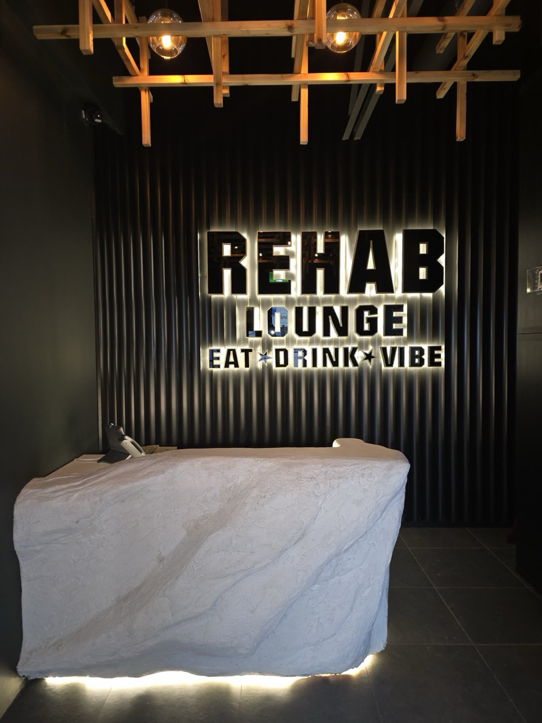 The Rehab Lounge entrance — backlit lettering over the stone host desk